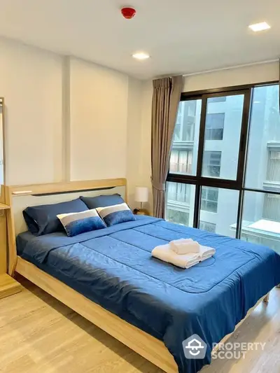 Modern bedroom with large window and stylish blue bedding in a contemporary apartment.