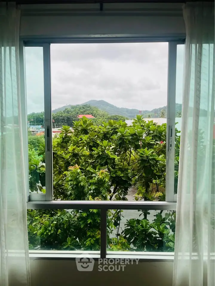 Scenic view from a window overlooking lush greenery and distant hills, perfect for nature lovers.