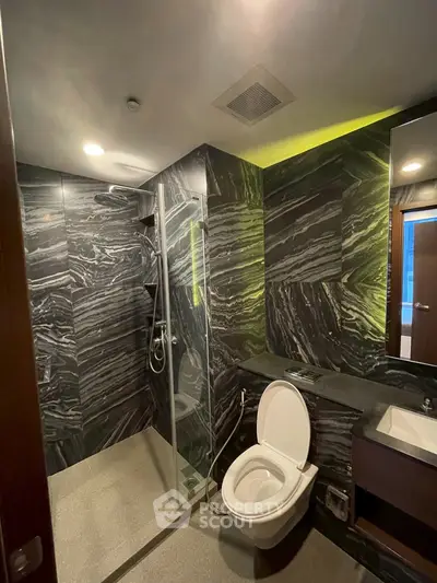 Luxurious modern bathroom with sleek black marble tiles and glass shower enclosure.