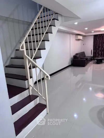 Spacious modern living room with sleek staircase and glossy flooring, perfect for contemporary living.