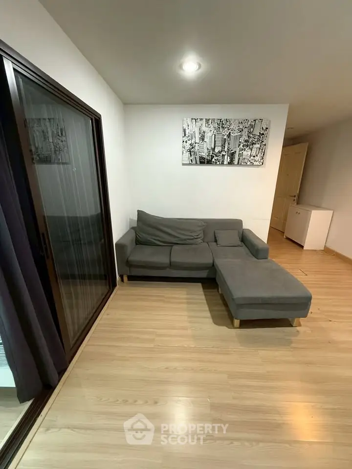 Modern living room with sleek gray sofa and wooden flooring, featuring a stylish cityscape artwork.