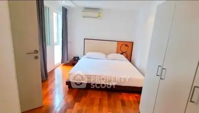 Spacious bedroom with wooden flooring and modern furnishings in a bright apartment.