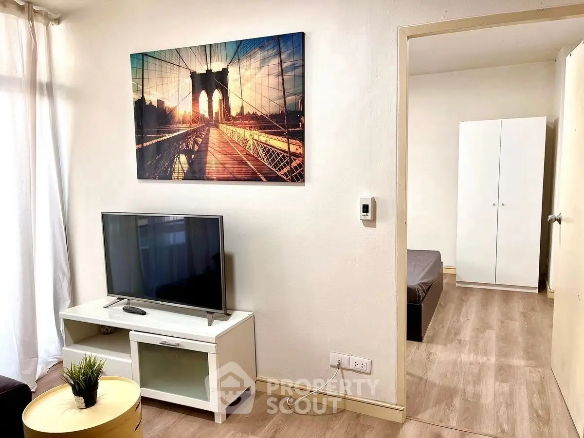 Cozy living room with modern decor and TV, leading to a minimalist bedroom.