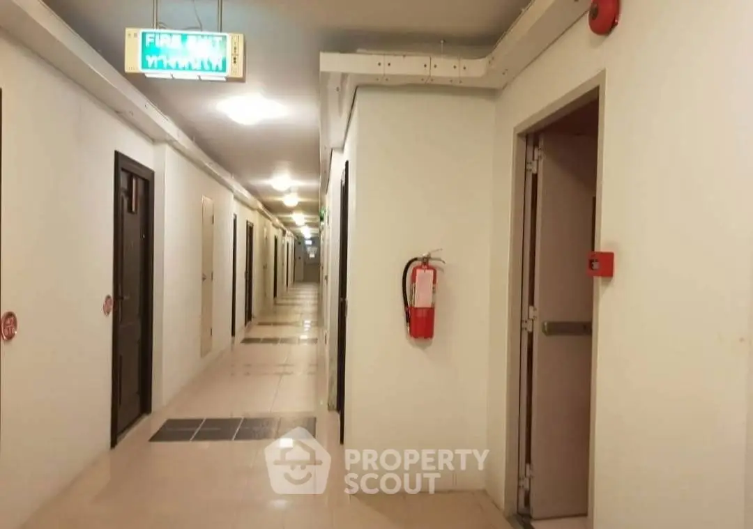 Spacious corridor in modern building with emergency exit sign and fire extinguisher.