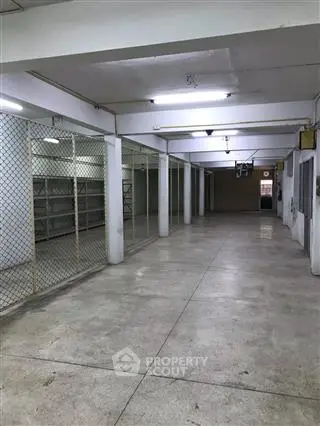 Spacious industrial storage area with concrete flooring and metal mesh partitions.