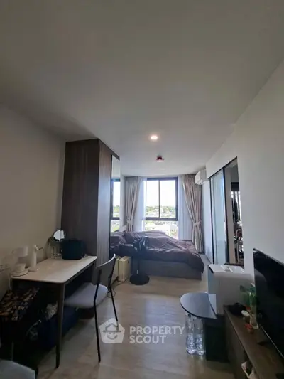 Modern studio apartment with cozy bedroom and workspace, featuring large windows and stylish decor.