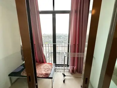 Cozy bedroom with balcony and city view, featuring large windows and pink curtains.