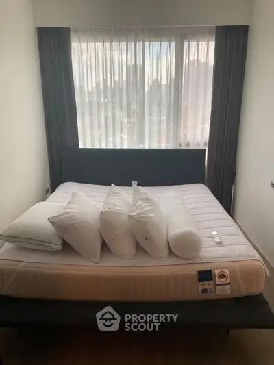 Cozy bedroom with a large bed and city view through sheer curtains, perfect for relaxation.
