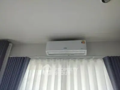 Modern air conditioning unit installed above window with elegant curtains in a bright room.