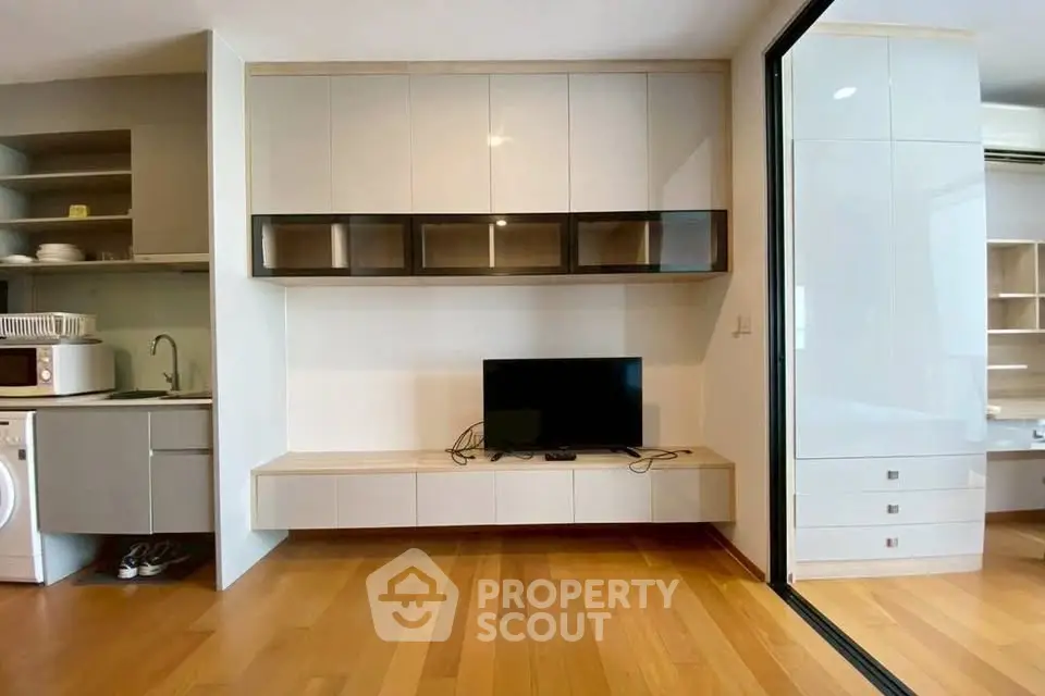 Modern living room with sleek cabinetry and hardwood floors, featuring a compact kitchen area with appliances.