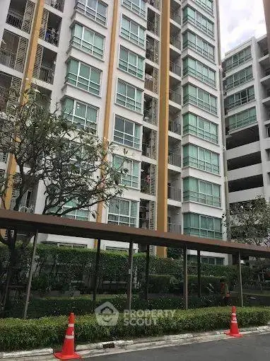 Modern high-rise residential building with lush greenery and glass facade.