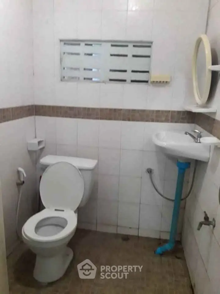 Compact bathroom with toilet, sink, and small window in tiled setting.