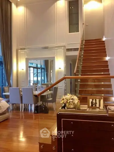 Luxurious duplex living room with elegant staircase and dining area, featuring high ceilings and modern decor.