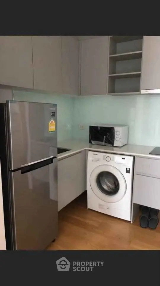 Modern kitchen with sleek appliances including fridge, washing machine, and microwave in compact layout.