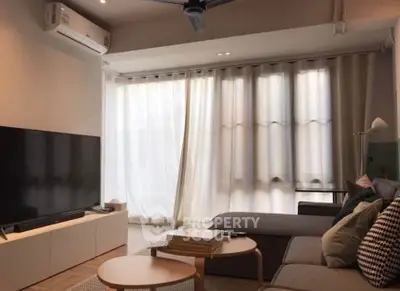 Modern living room with large TV, cozy sofa, and natural light through sheer curtains.