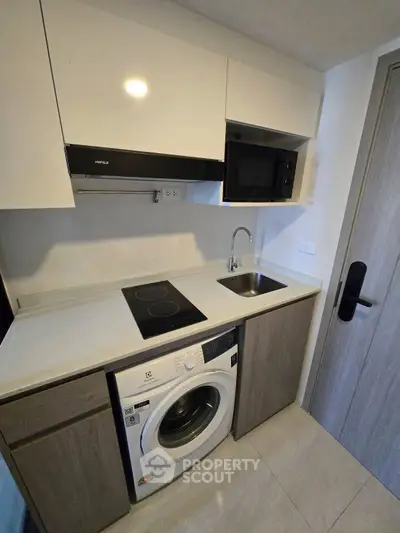 Compact modern kitchen with washing machine and microwave in sleek apartment.