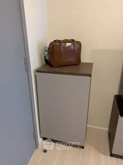 Compact storage cabinet in modern apartment corner with stylish brown leather bag on top.