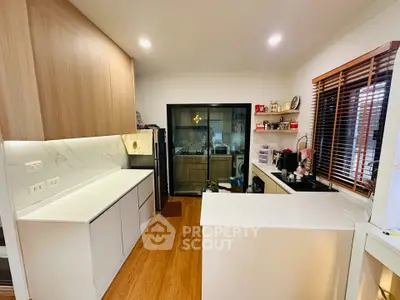 Modern kitchen with sleek white cabinets and wooden flooring, featuring an open layout and stylish lighting.