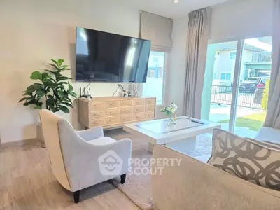 Modern living room with large TV, stylish furniture, and natural light from sliding glass doors.