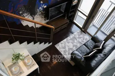 Modern living room with stylish decor, featuring a black leather sofa, geometric rug, and artistic wall design.