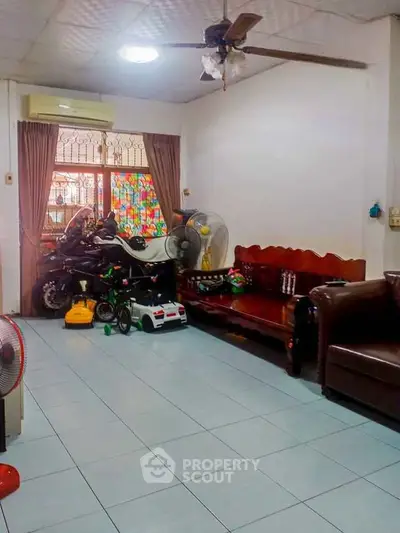 Spacious living room with tiled floor and ceiling fan, featuring cozy seating and children's toys.