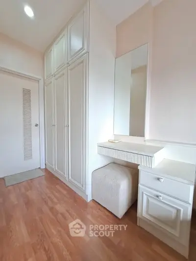 Elegant bedroom with built-in wardrobe and vanity, featuring wooden flooring and soft lighting.