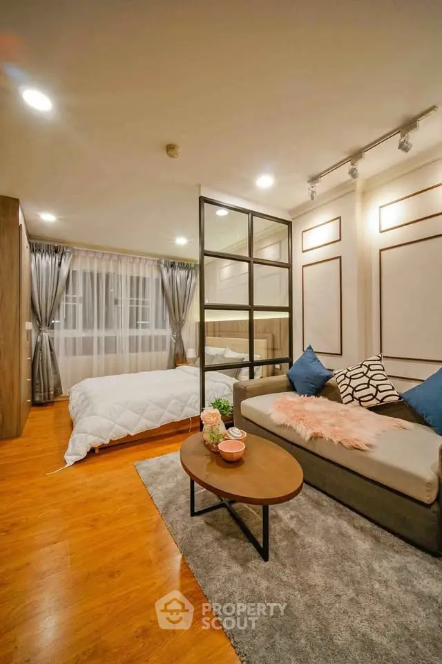 Modern studio apartment with cozy living area and stylish bedroom separated by glass partition.