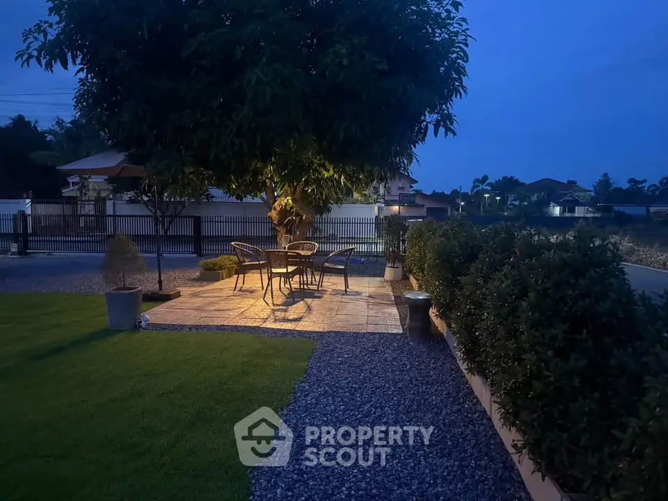 Charming outdoor patio with elegant seating under a tree, perfect for evening relaxation in a serene garden setting.