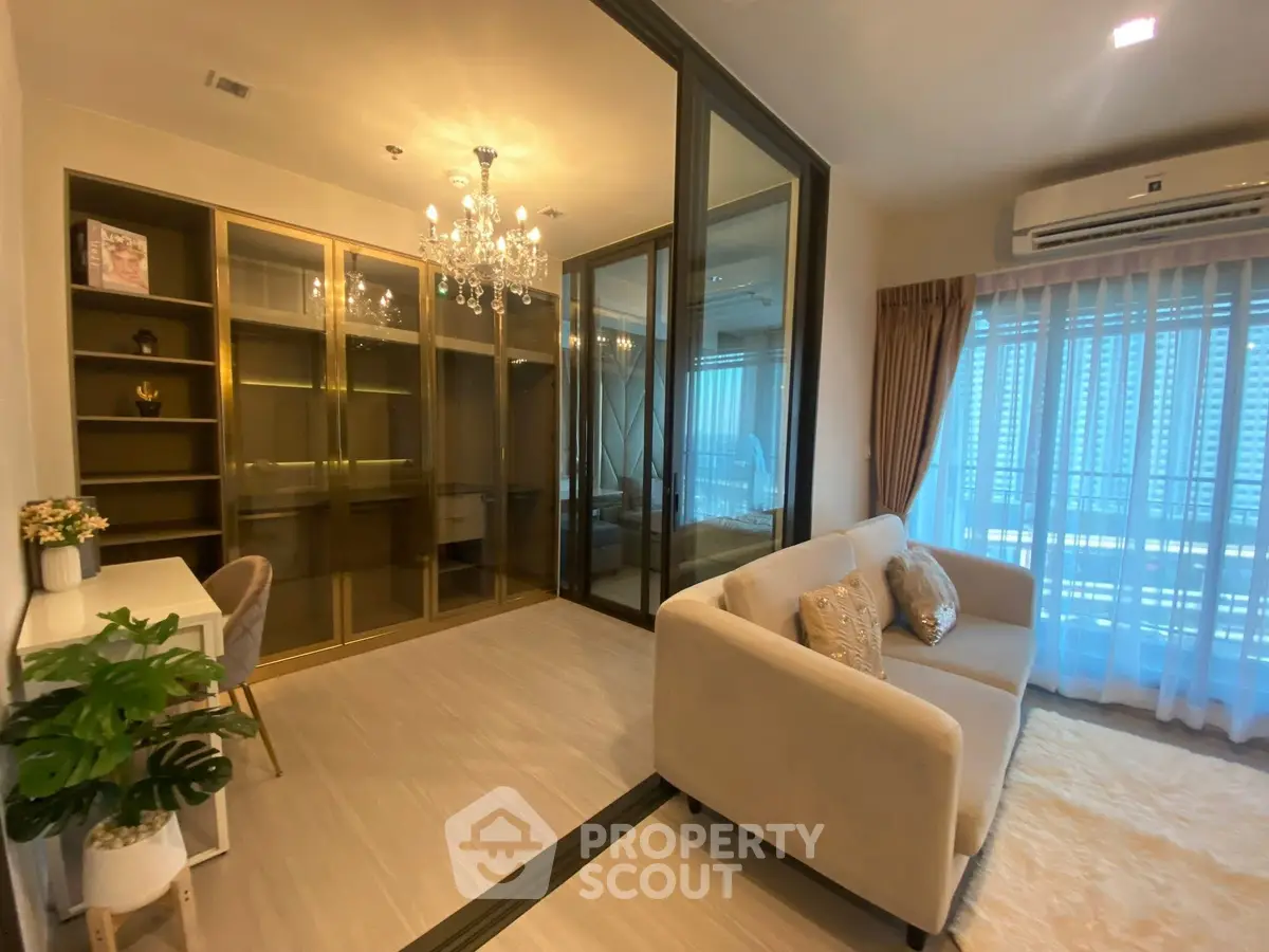 Luxurious living room with elegant chandelier and glass doors leading to a cozy study area.