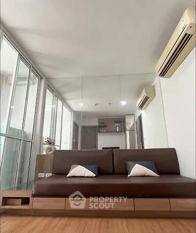 Modern living room with sleek brown sofa and mirrored wall, featuring air conditioning and wooden flooring.
