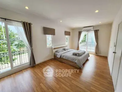Spacious bedroom with large windows and balcony access, featuring elegant wooden flooring and modern decor.
