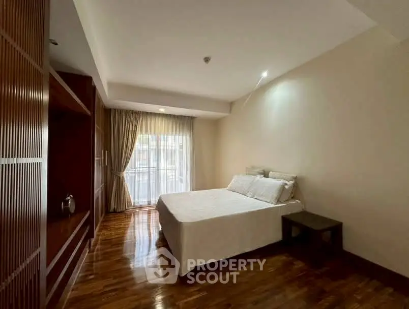 Spacious bedroom with wooden flooring and large window for natural light