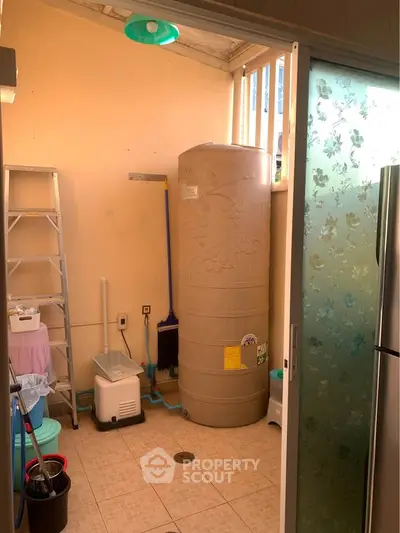 Utility room with water tank and storage ladder in a well-lit corner.