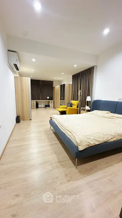 Spacious modern bedroom with stylish decor and ample natural light, featuring a cozy seating area and sleek wooden flooring.