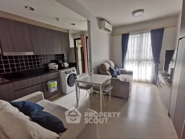 Modern open-plan living room with kitchen, featuring sleek cabinetry and natural light.