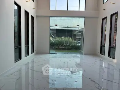 Spacious modern living room with high ceilings and large windows, featuring elegant marble flooring.