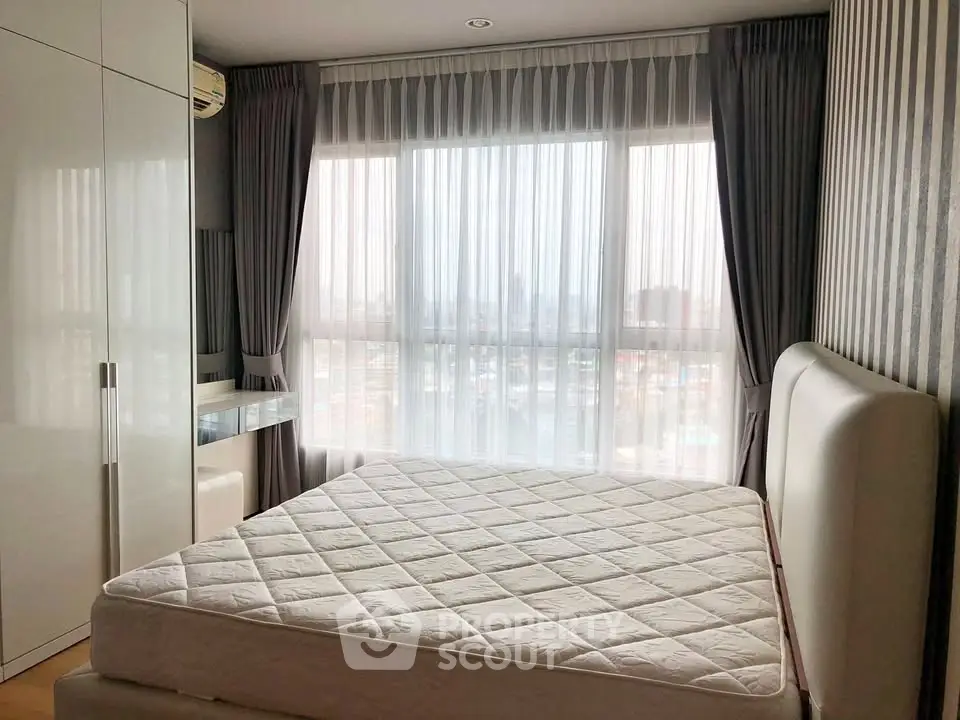Modern bedroom with large window and city view, featuring sleek furniture and elegant curtains.