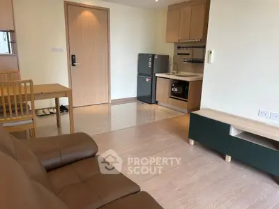 Modern open-layout living room with kitchen, featuring sleek wooden furniture and compact appliances.