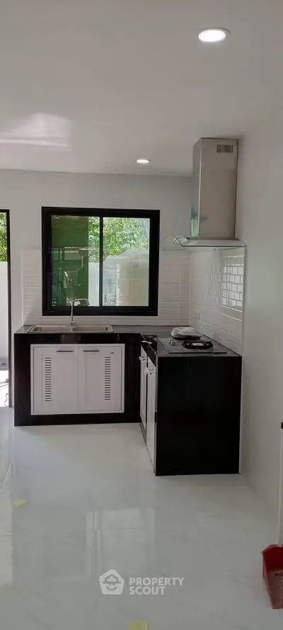 Modern kitchen with sleek black and white design, featuring gas stove and large window.