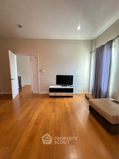 Spacious living room with wooden flooring and modern TV setup, perfect for relaxation.