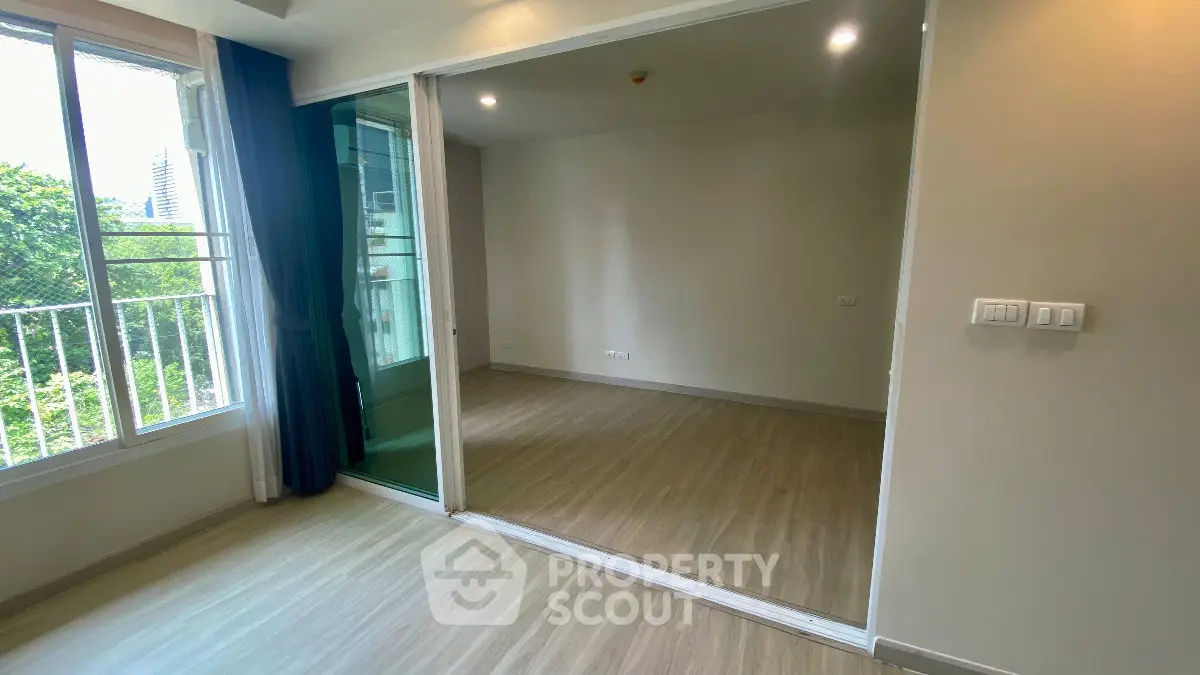 Spacious room with large windows and sliding glass doors leading to a balcony, offering a serene view.