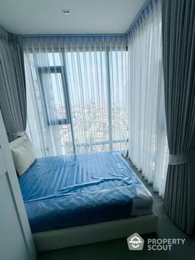 Modern bedroom with floor-to-ceiling windows and city view, featuring elegant curtains and a cozy bed.