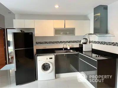 Modern kitchen with sleek black and white cabinetry, washing machine, and built-in appliances.