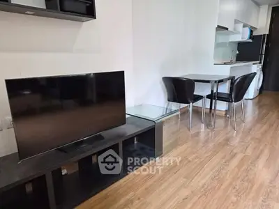 Modern living room with sleek TV setup and compact dining area in open layout apartment.