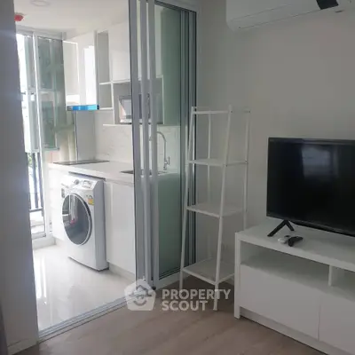 Modern apartment with compact kitchen and living area featuring washing machine and TV setup.