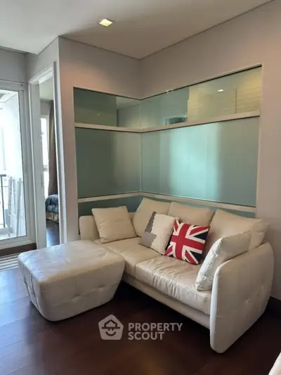 Stylish living room with modern white sofa and British flag pillow, featuring sleek glass shelving and wooden flooring.