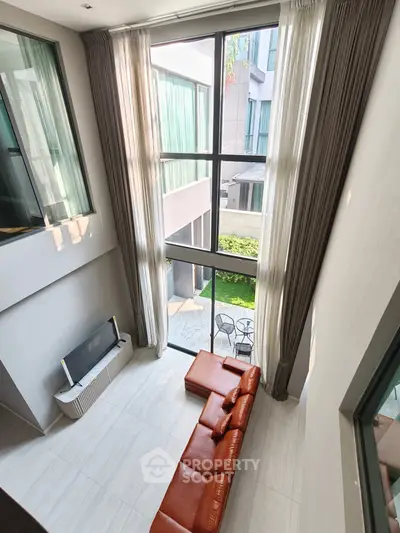 Spacious modern living room with high ceilings and large windows overlooking a garden patio.