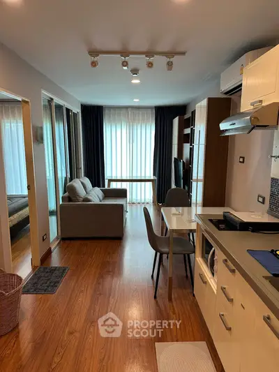 Modern open-plan living room with sleek kitchen and cozy seating area, featuring hardwood floors and natural light.