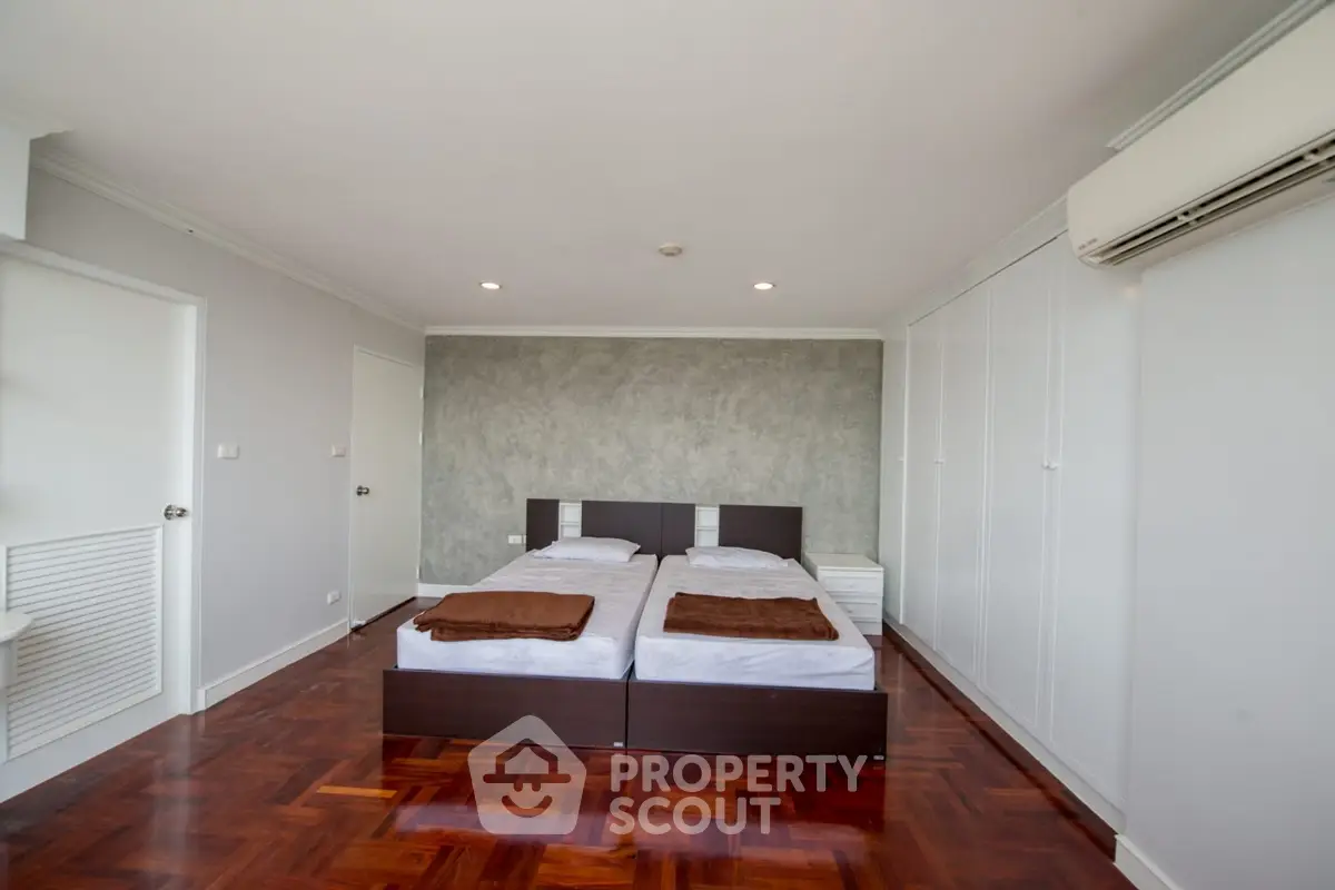 Spacious bedroom with twin beds and elegant wooden flooring in modern apartment.