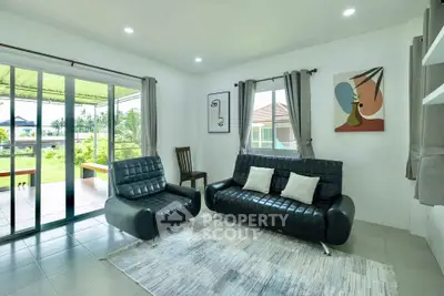 Modern living room with sleek black leather sofas and large windows opening to a garden view.
